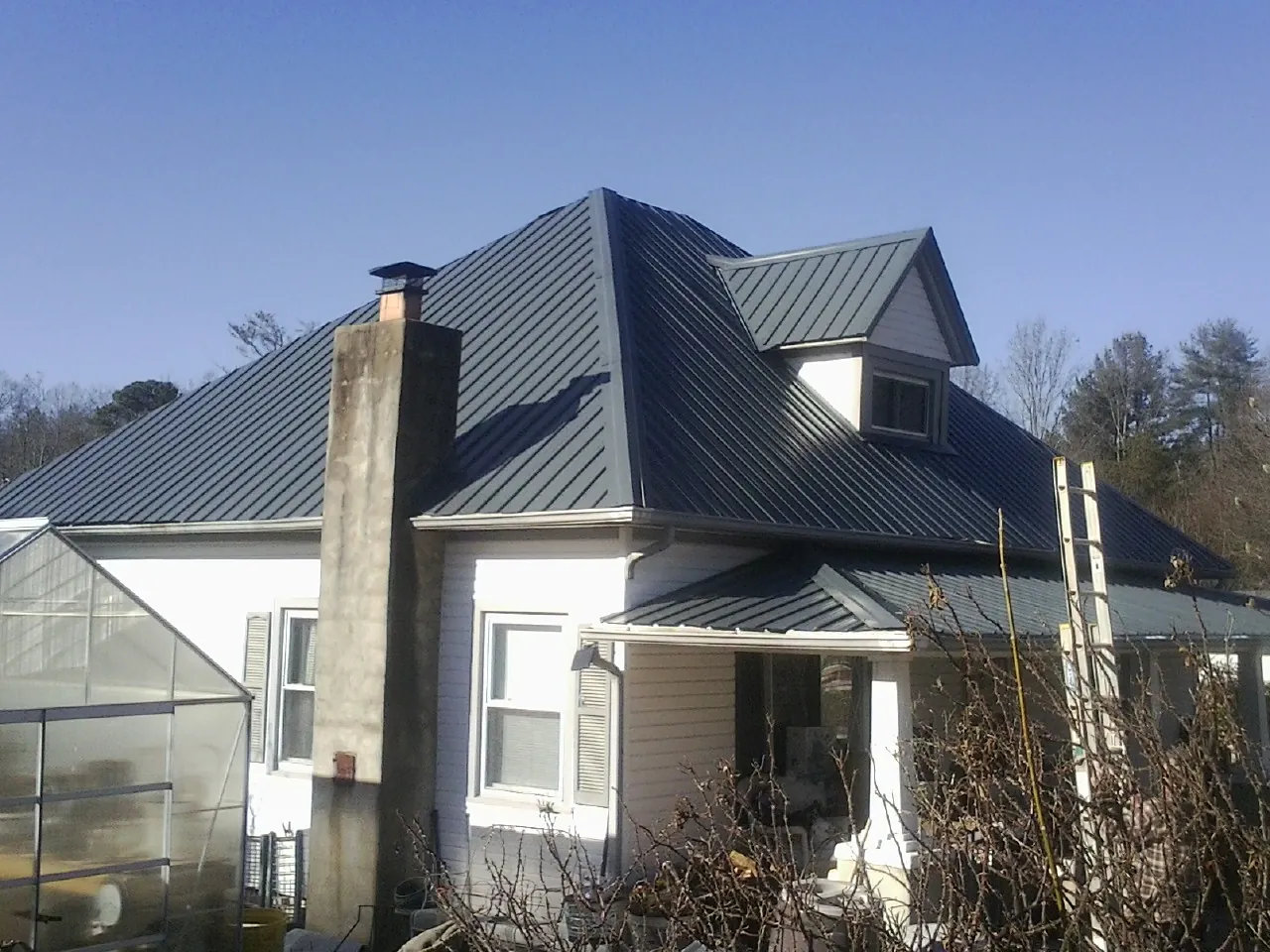 Dark blue standing seam metal roof on a white farmhouse with dormer — Slate & Tile Roof Repair by Roofing Brothers in Knob Noster