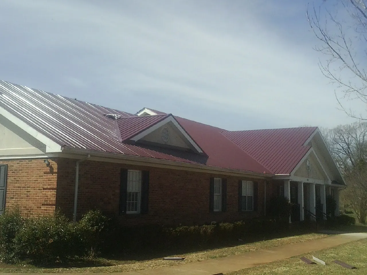 Red metal roof with gabled entries on a long brick building, from a Hail Damage Roof Repair job in Knob Noster