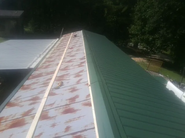 Old rusted panels beside newly installed green metal roofing — Wind Damage Roof Repair by Roofing Brothers in Knob Noster