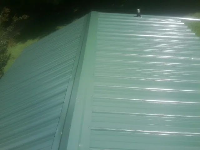 New green metal panels meeting at the ridge of a roof — Flat Roof Repair work by our crew in Knob Noster