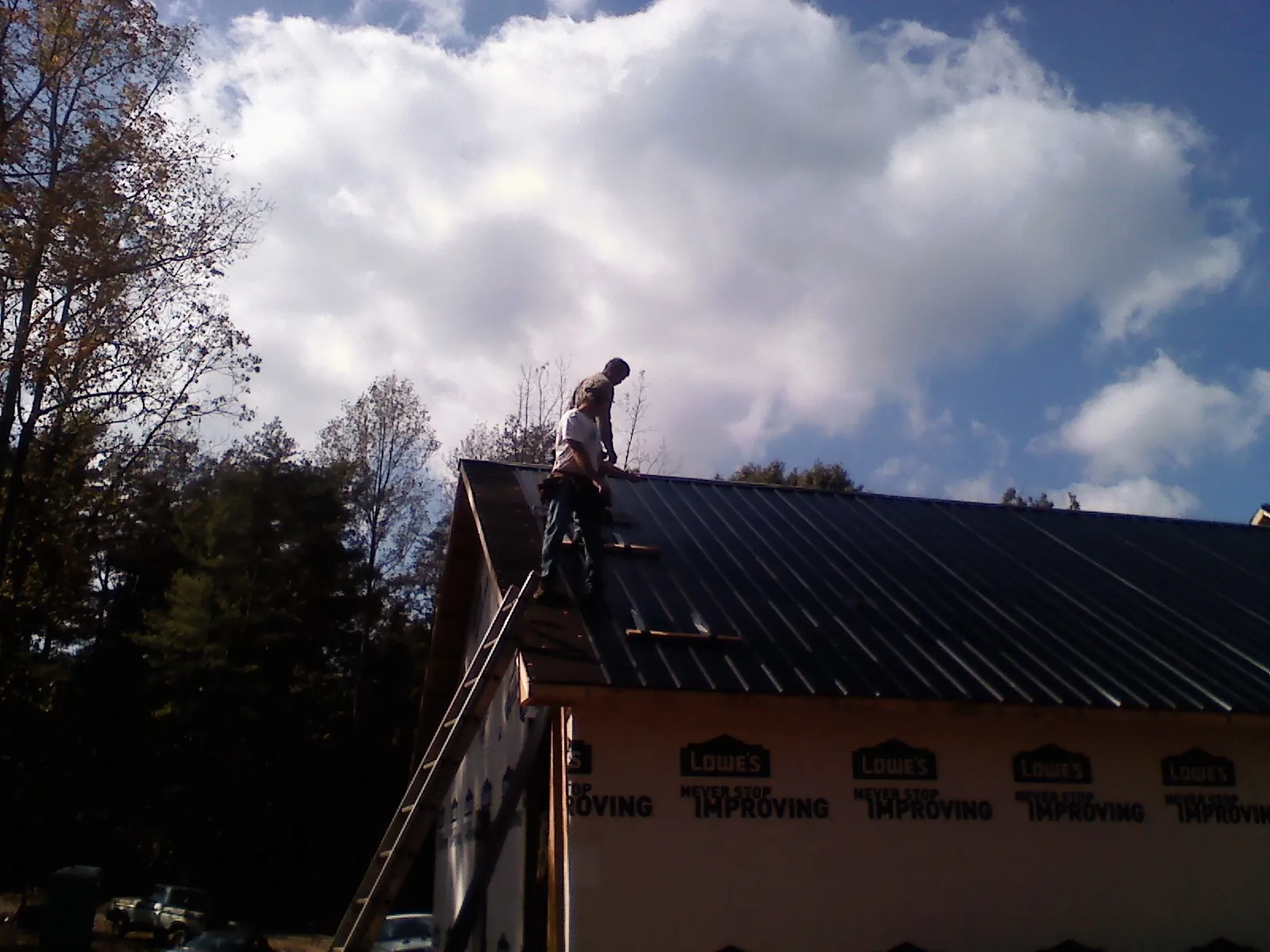 Roofer fastening dark metal panels high against a cloudy sky, from a Roof Inspection job in Knob Noster