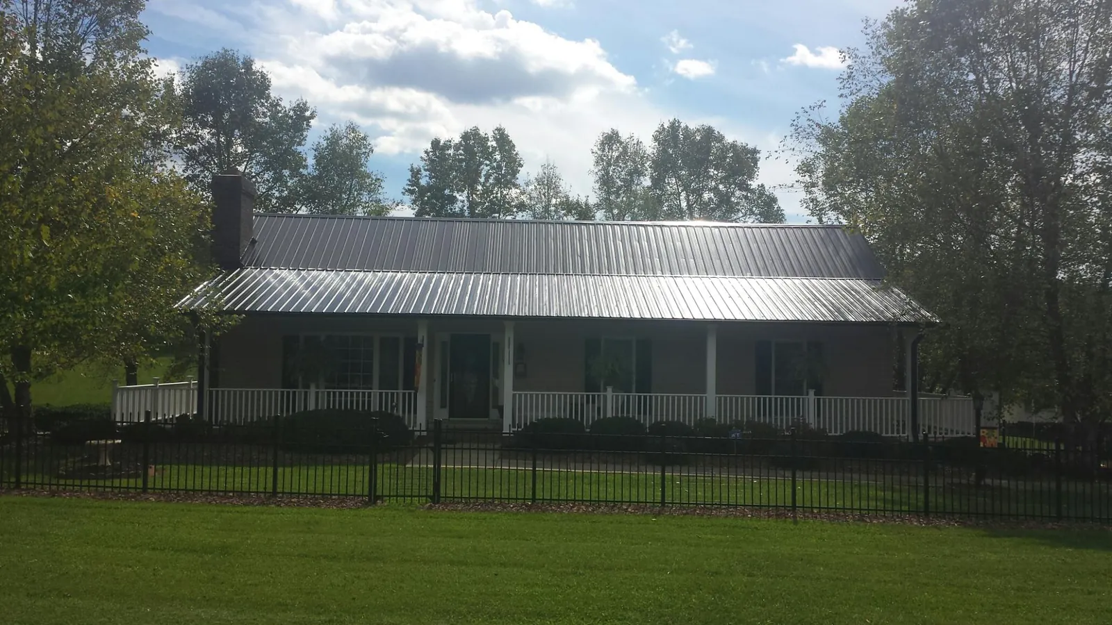 Gray metal roof on a brick ranch with a full width front porch — Gutter Guard Installation work by our crew in Knob Noster