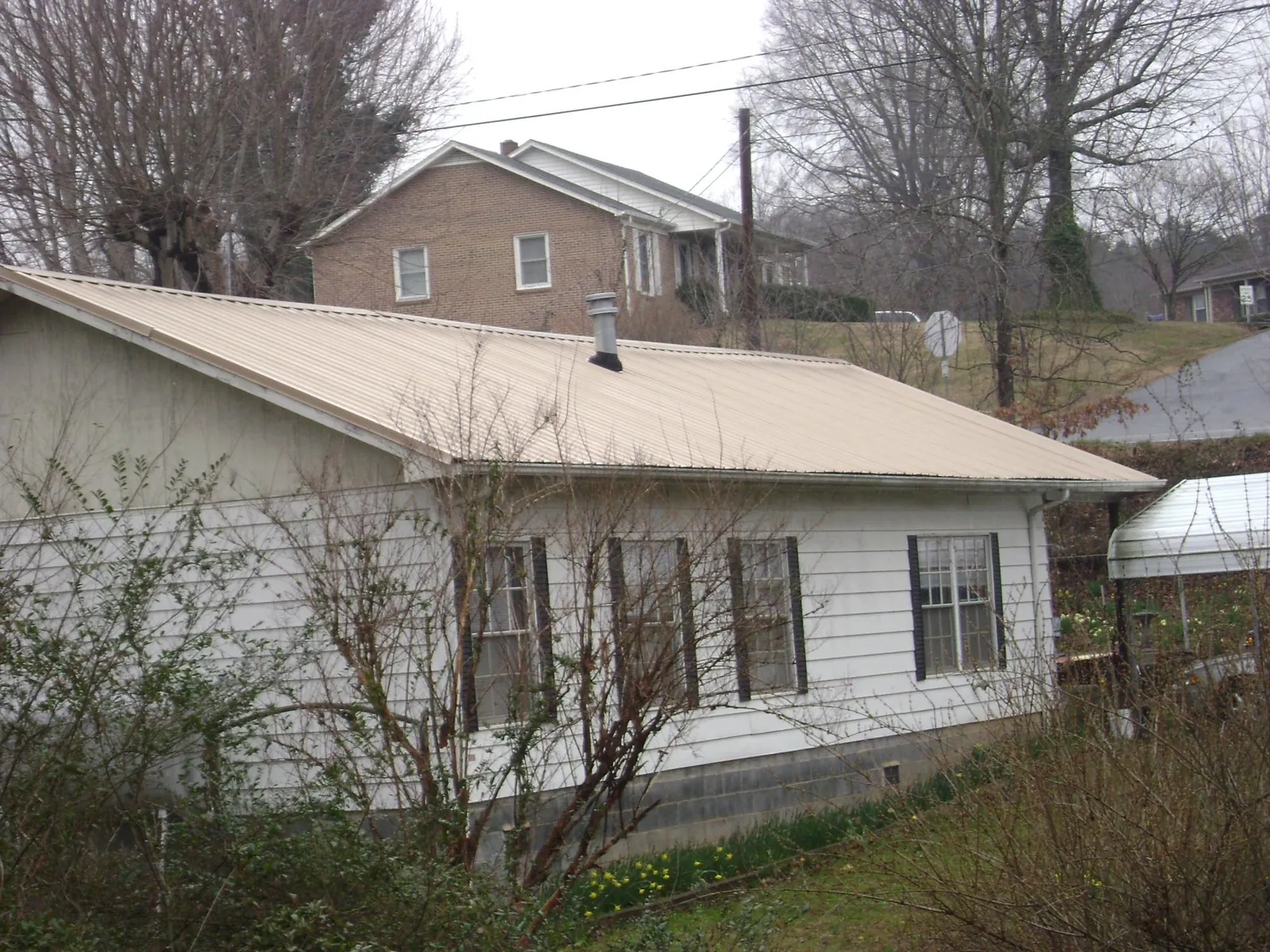 Tan metal roof on a white sided house set into a hillside — Commercial Roofing by Roofing Brothers in Knob Noster