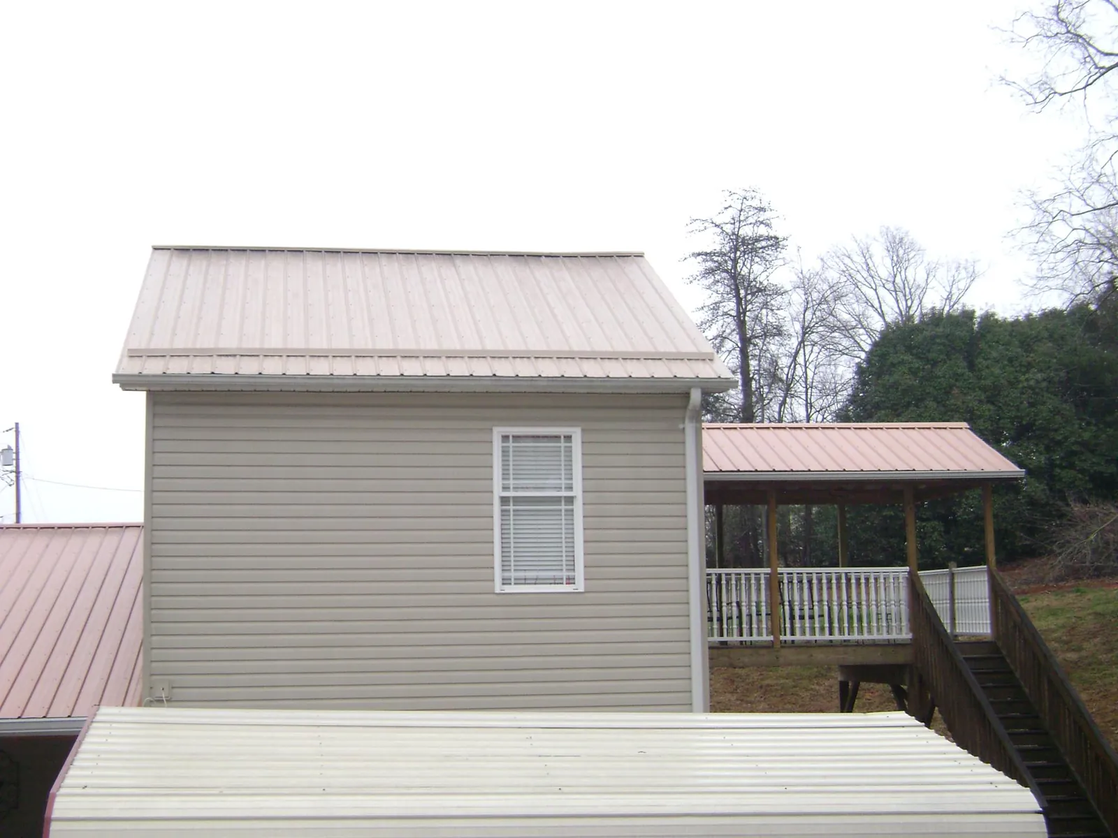 Tan metal roofs on a two story addition and attached porch, from a Roof Replacement job in Knob Noster